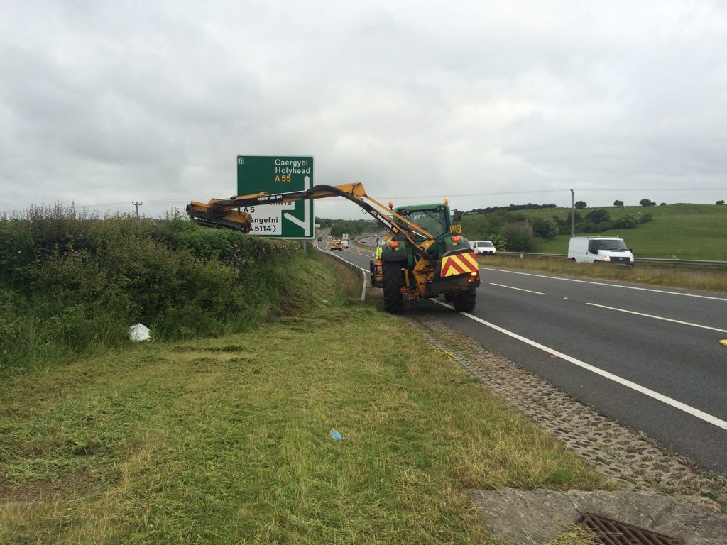 A tractor and operator trimming hedges on the A55 on Anglesey